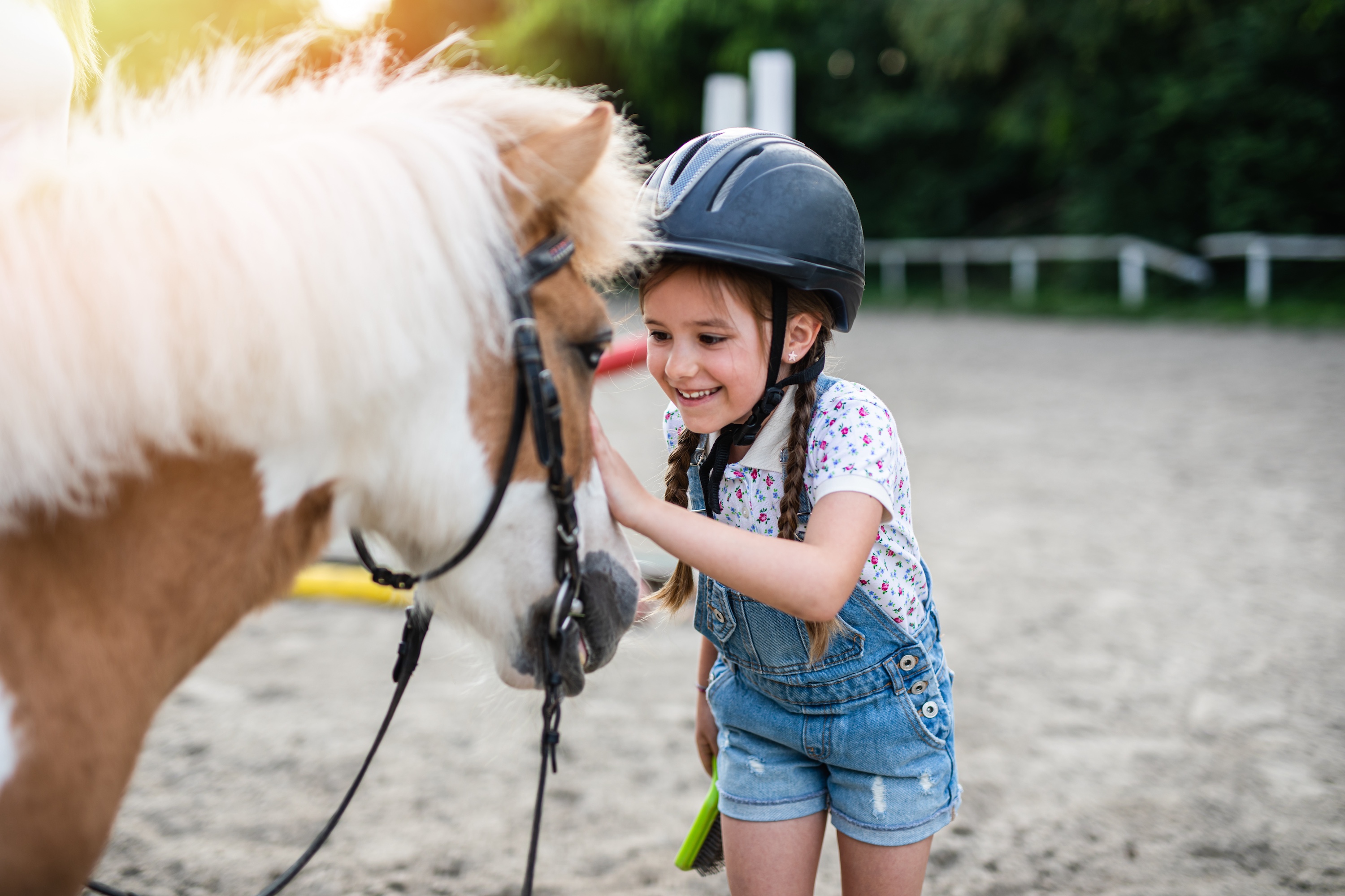 Mädchen mit Reithelm streichelt ein geschecktes Pony auf dem Reitplatz