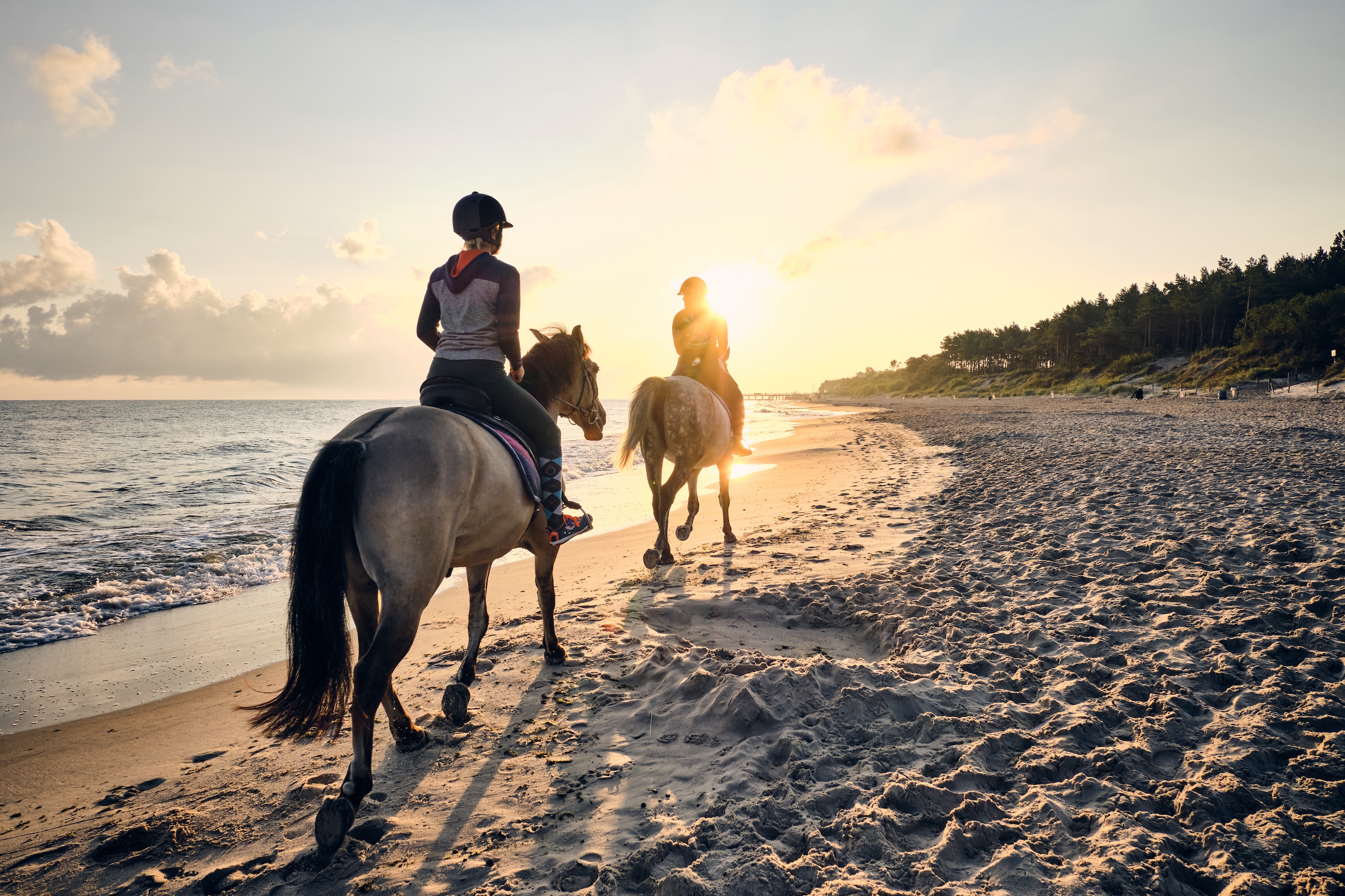 zwei Frauen reiten am Strand im Sonnenuntergang